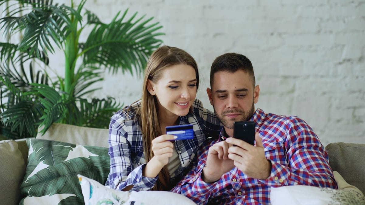 Two adults at home checking a payment on a phone with a bank card